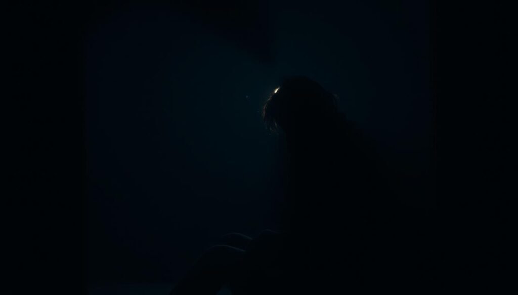 A person, consumed by an uncontrollable urge, sits alone in a dimly lit room, their face obscured by shadows. The atmosphere is somber, with a sense of anguish and isolation. The lighting is low-key, creating dramatic shadows and highlights, emphasizing the emotional turmoil. The camera angle is slightly elevated, lending a sense of vulnerability and introspection. The background is blurred, keeping the focus on the central figure, who appears lost in a cycle of compulsive behavior, their body language reflecting the inner struggle.
